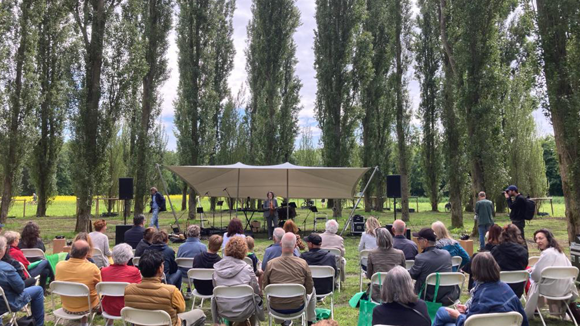 Foto: toeschouwers zitten op een grasveld op stoelen en kijken naar voorstelling